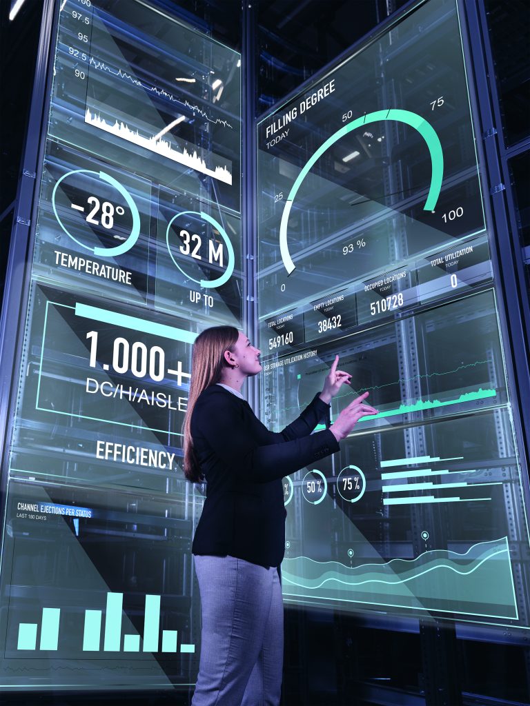 Een vrouw in zakelijke kleding interageert met grote transparante digitale schermen die gegevens, grafieken en diagrammen weergeven over temperatuur, capaciteit, efficiëntie en statistieken in een futuristische hightech omgeving.