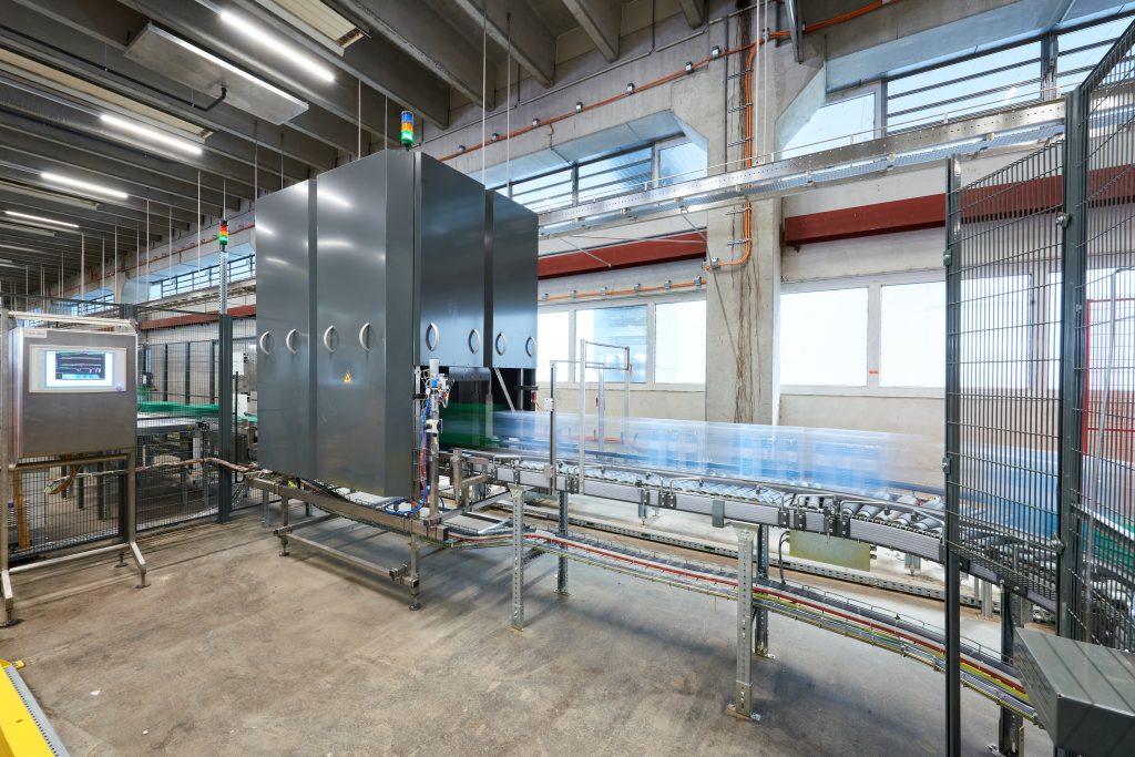 Cleanaway visual nl Een moderne industriële bottelarij met geautomatiseerde machines en transportbanden die heldere flessen op hoge snelheid verplaatsen in een ruime, goed verlichte fabriek.