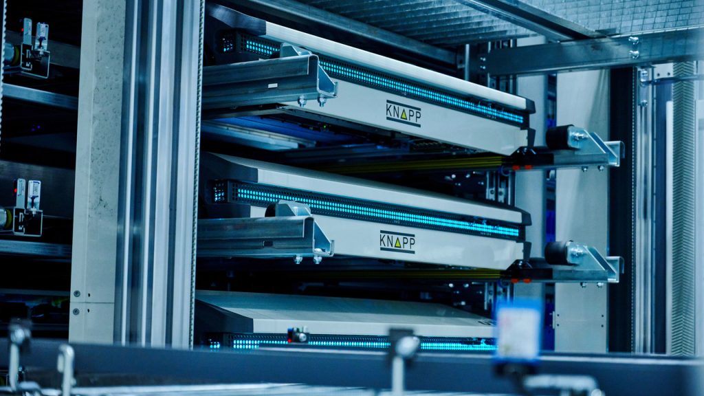Close-up van een automatisch magazijnsysteem van KNAPP in de sectorindustrie, met transportbanden en metalen rekken voor efficiënt sorteren en transporteren van goederen.
