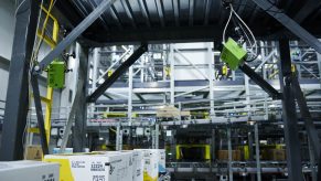 spar - visual 4 Een blik in een geautomatiseerd magazijn toont transportbanden, robotsystemen, kartonnen dozen en machines boven het hoofd, wat een moderne, industriële omgeving voor geautomatiseerd sorteren en logistiek benadrukt.